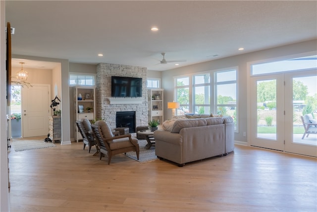 living room with a stone fireplace, ceiling fan with notable chandelier, plenty of natural light, and light hardwood / wood-style flooring