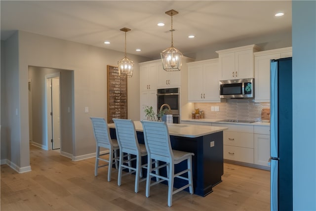 kitchen with pendant lighting, a center island with sink, light hardwood / wood-style flooring, white cabinetry, and appliances with stainless steel finishes