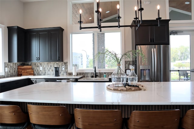 kitchen featuring pendant lighting, stainless steel refrigerator with ice dispenser, a kitchen bar, and sink