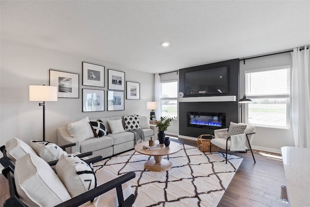 living area with a glass covered fireplace, wood finished floors, baseboards, and a textured ceiling