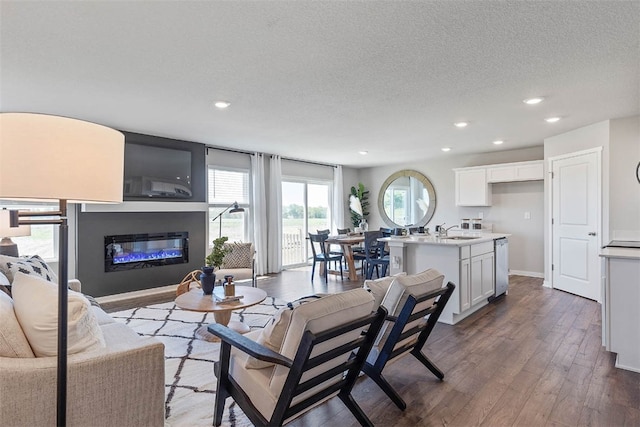 living area with baseboards, recessed lighting, wood finished floors, a glass covered fireplace, and a textured ceiling