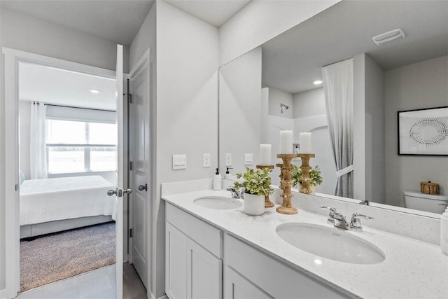 ensuite bathroom with double vanity, connected bathroom, toilet, and a sink