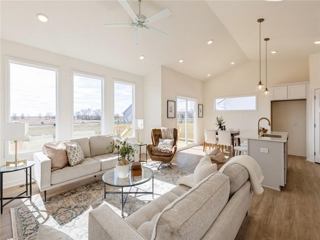 living room featuring light wood-type flooring, high vaulted ceiling, ceiling fan, and sink