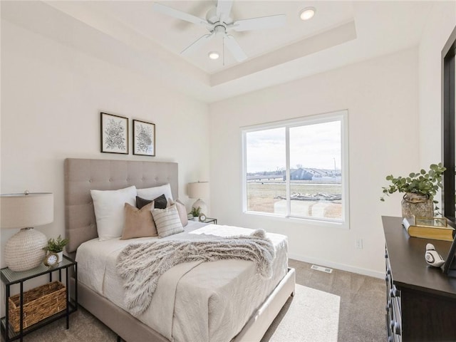 bedroom with ceiling fan, a raised ceiling, and light carpet