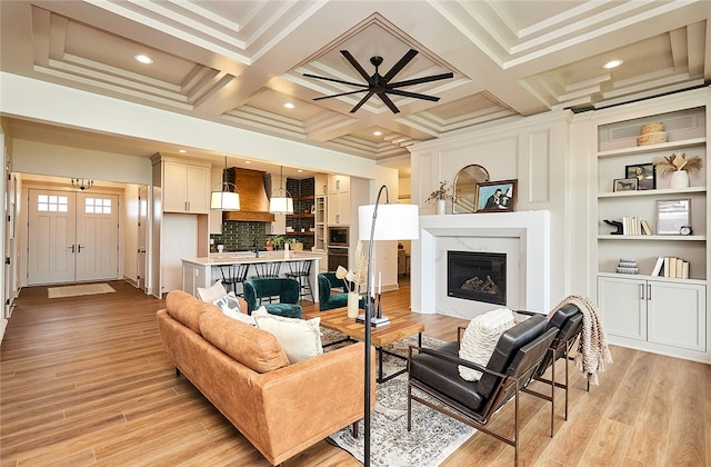 living room featuring beamed ceiling, coffered ceiling, a high end fireplace, and light hardwood / wood-style floors