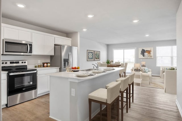 kitchen featuring white cabinets, a center island with sink, appliances with stainless steel finishes, and a kitchen bar