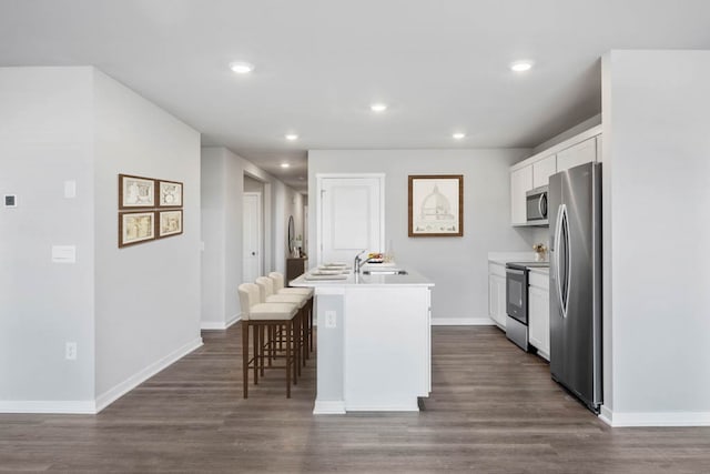 kitchen featuring a kitchen island with sink, stainless steel appliances, a breakfast bar, dark hardwood / wood-style floors, and white cabinetry