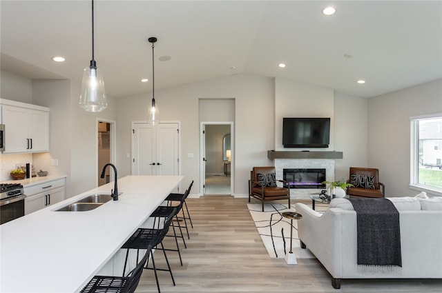 kitchen with sink, hanging light fixtures, light hardwood / wood-style flooring, vaulted ceiling, and white cabinetry