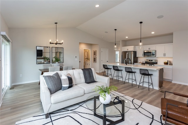 living room with light wood-type flooring, an inviting chandelier, and lofted ceiling