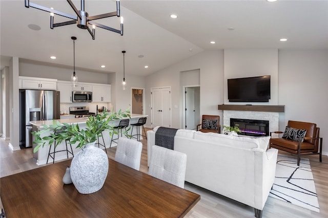 dining space featuring a fireplace, light hardwood / wood-style floors, vaulted ceiling, and an inviting chandelier