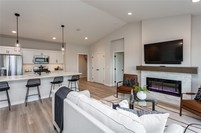 living room featuring a stone fireplace, light wood-type flooring, sink, and vaulted ceiling