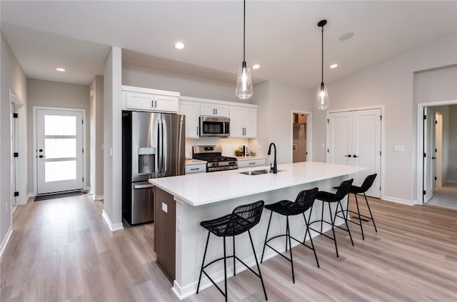 kitchen featuring white cabinets, an island with sink, appliances with stainless steel finishes, decorative light fixtures, and a kitchen bar