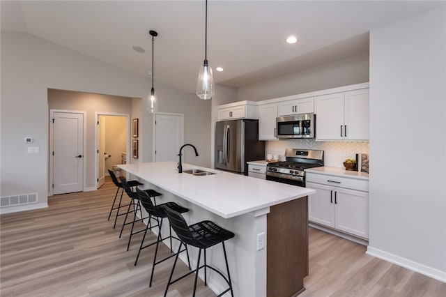 kitchen with a kitchen island with sink, sink, vaulted ceiling, appliances with stainless steel finishes, and white cabinetry