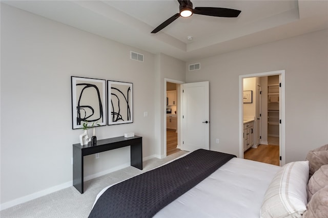 carpeted bedroom featuring a raised ceiling, ceiling fan, and ensuite bathroom