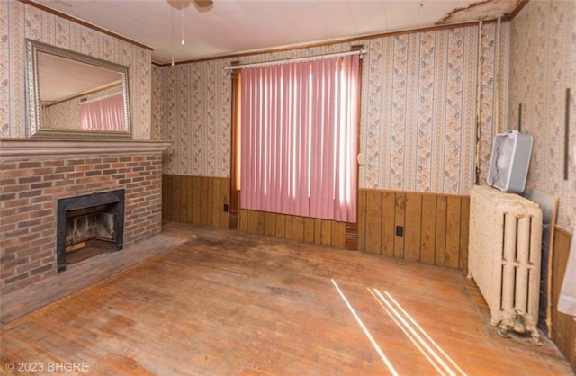 unfurnished living room with ornamental molding, radiator heating unit, hardwood / wood-style floors, and a brick fireplace