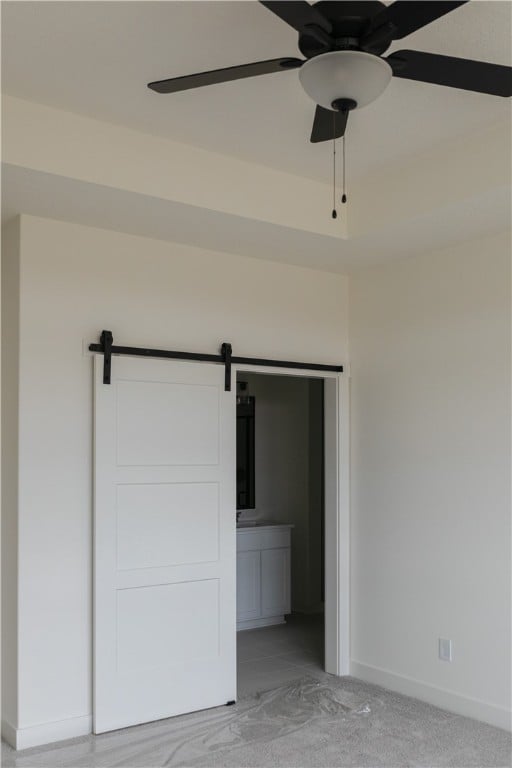 unfurnished bedroom featuring a barn door, connected bathroom, ceiling fan, and light colored carpet