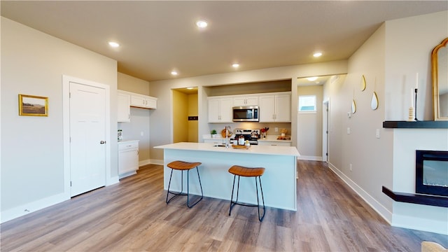 kitchen featuring appliances with stainless steel finishes, white cabinetry, a kitchen island with sink, and light wood-type flooring