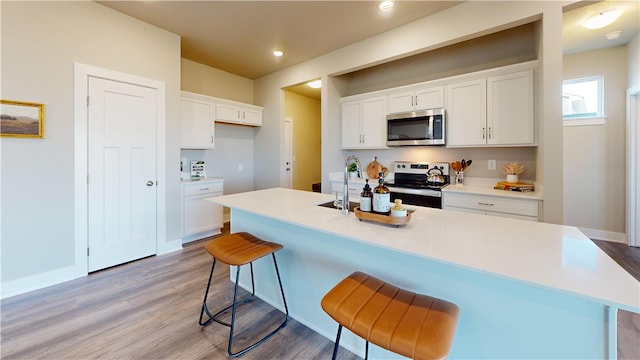 kitchen with appliances with stainless steel finishes, light wood-type flooring, a center island with sink, and white cabinets