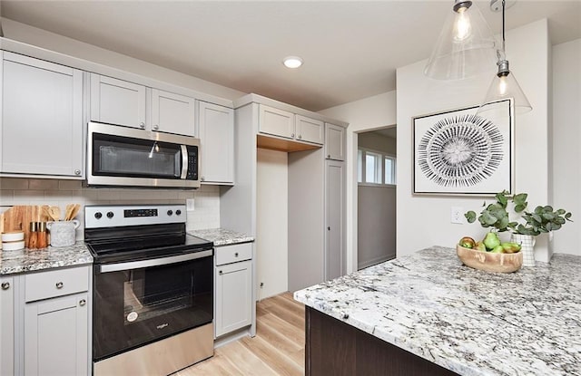 kitchen with light wood-type flooring, backsplash, stainless steel appliances, and hanging light fixtures