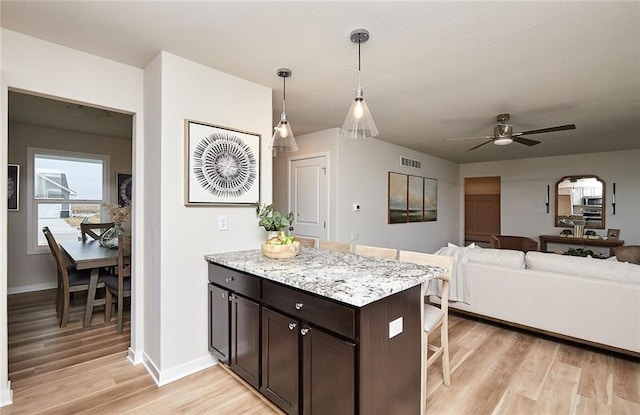 kitchen featuring light stone countertops, a breakfast bar, dark brown cabinets, decorative light fixtures, and light hardwood / wood-style floors