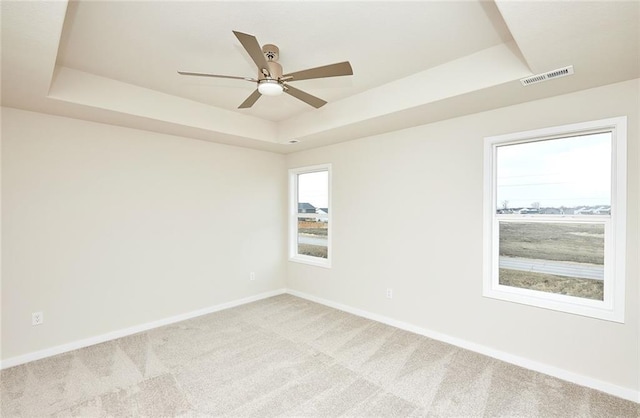 empty room featuring light carpet, a raised ceiling, and ceiling fan