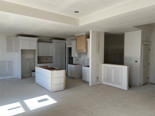 kitchen with white cabinetry, decorative backsplash, a kitchen island, and a textured ceiling