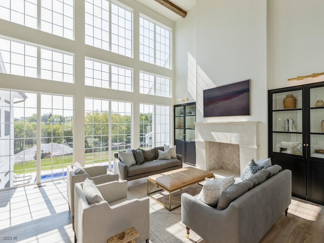 living room featuring beam ceiling, a towering ceiling, wood finished floors, and a high end fireplace