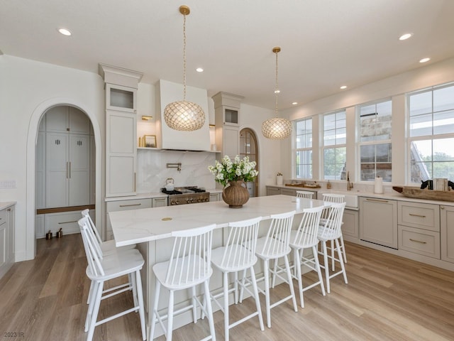 kitchen featuring light wood finished floors, decorative backsplash, glass insert cabinets, and a sink