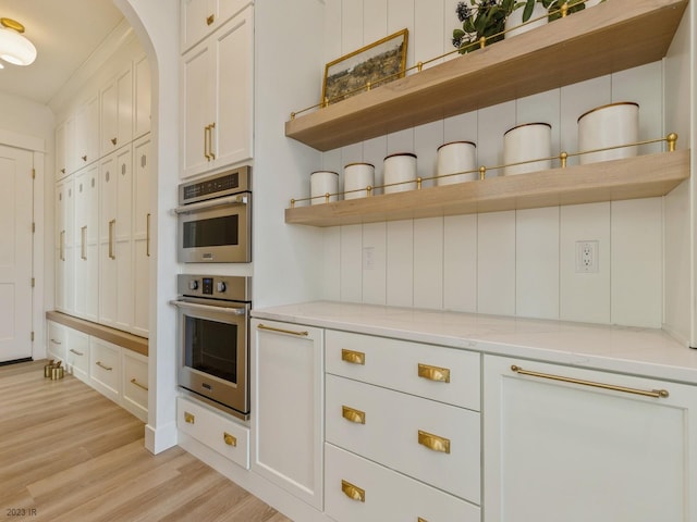 kitchen featuring white cabinets, stainless steel double oven, light wood-type flooring, and light stone countertops