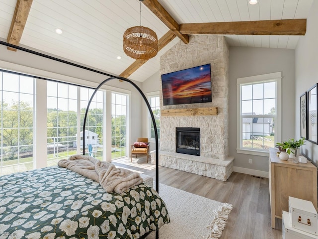 bedroom with light wood-type flooring, vaulted ceiling with beams, and a stone fireplace