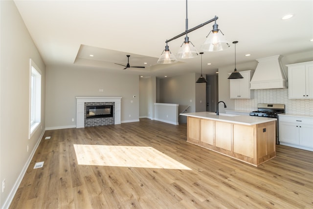 kitchen featuring white cabinets, pendant lighting, a kitchen island with sink, custom range hood, and light hardwood / wood-style floors