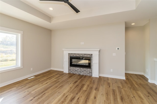 unfurnished living room featuring light wood-type flooring, a tray ceiling, and ceiling fan