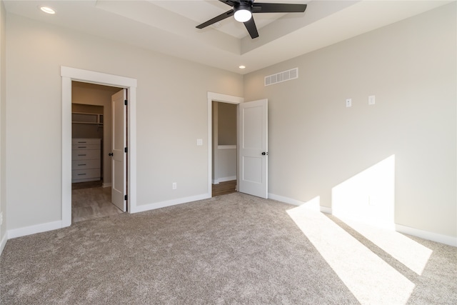 unfurnished bedroom with light carpet, ceiling fan, a walk in closet, and a closet