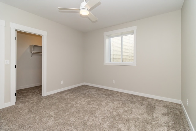 unfurnished bedroom featuring a spacious closet, light carpet, a closet, and ceiling fan