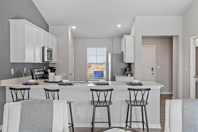 kitchen with stainless steel appliances, sink, white cabinetry, kitchen peninsula, and a breakfast bar area