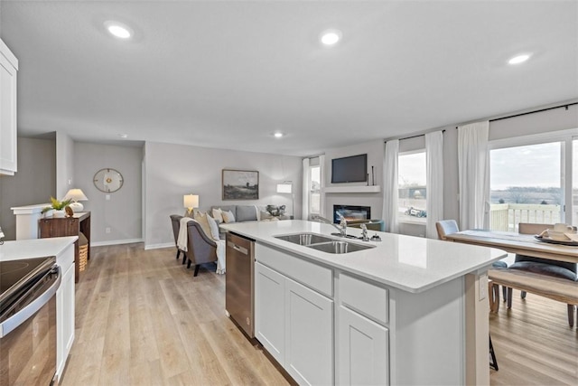 kitchen with white cabinetry, appliances with stainless steel finishes, an island with sink, sink, and light hardwood / wood-style flooring