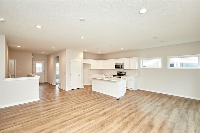 kitchen with appliances with stainless steel finishes, light wood-type flooring, a textured ceiling, a kitchen island with sink, and white cabinetry