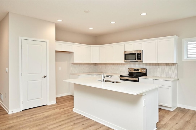 kitchen with appliances with stainless steel finishes, light wood-type flooring, a kitchen island with sink, sink, and white cabinets