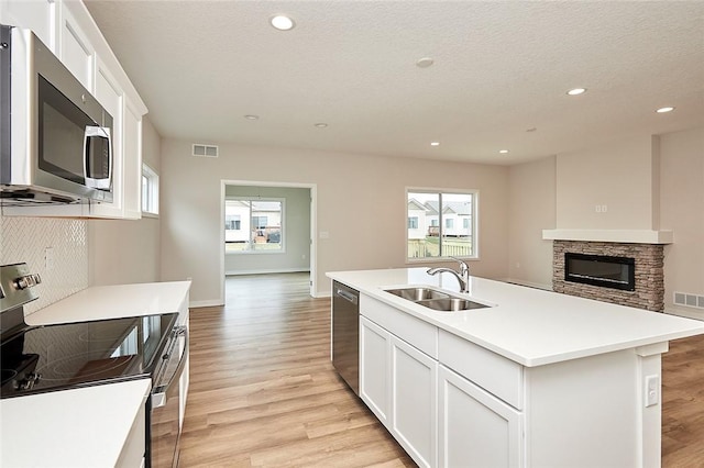 kitchen with sink, a textured ceiling, a kitchen island with sink, appliances with stainless steel finishes, and light wood-type flooring