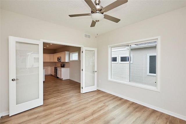 empty room featuring ceiling fan, light wood-type flooring, a textured ceiling, and french doors