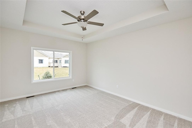 carpeted empty room with a raised ceiling and ceiling fan