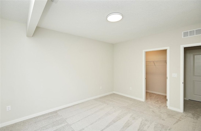 unfurnished bedroom featuring beam ceiling, a spacious closet, light colored carpet, a textured ceiling, and a closet