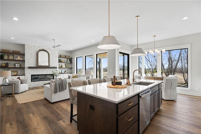 kitchen featuring a stone fireplace, a kitchen island with sink, dark brown cabinetry, light countertops, and dishwasher