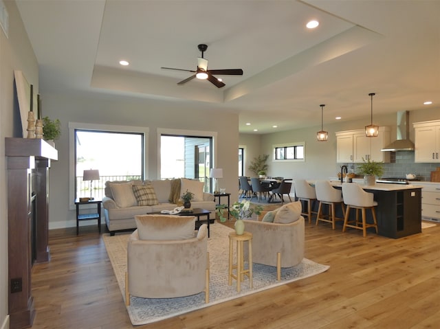 living room with a raised ceiling, a healthy amount of sunlight, hardwood / wood-style floors, and ceiling fan