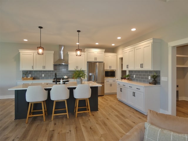 kitchen with wall chimney exhaust hood, light hardwood / wood-style flooring, appliances with stainless steel finishes, and a center island with sink