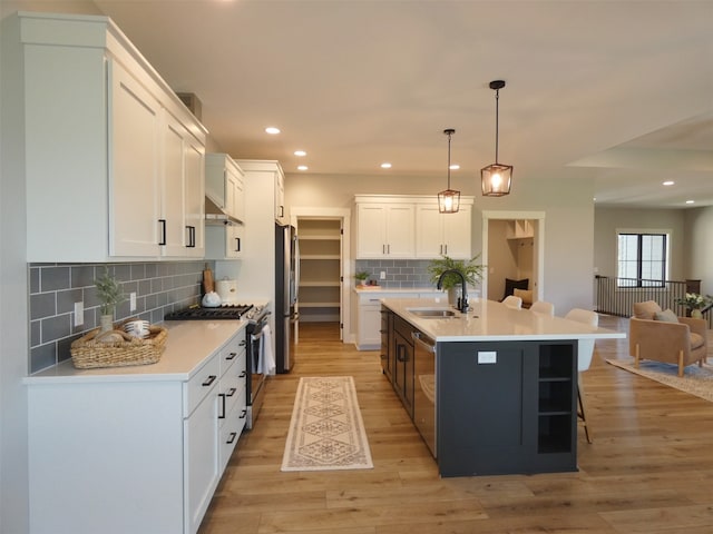 kitchen with a kitchen island with sink, white cabinetry, backsplash, stainless steel appliances, and sink