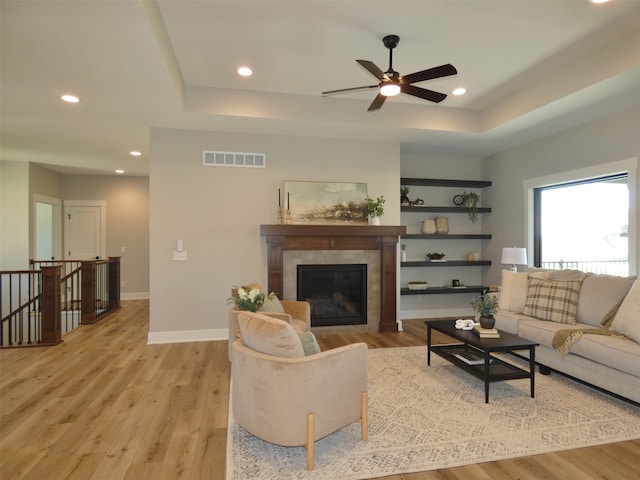 living room with ceiling fan, a fireplace, light hardwood / wood-style floors, and a raised ceiling