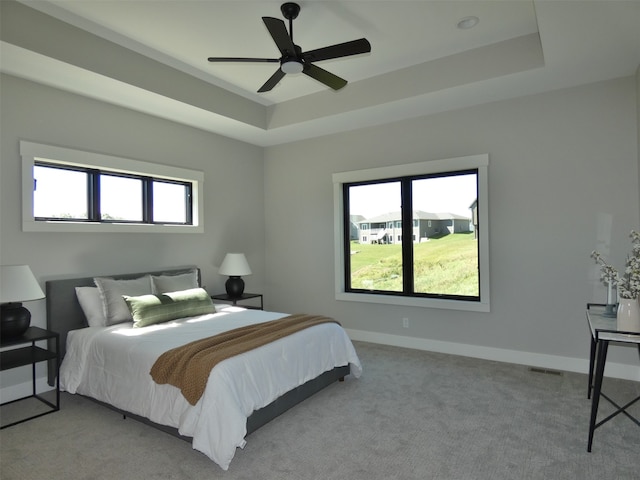 carpeted bedroom with a tray ceiling, multiple windows, and ceiling fan