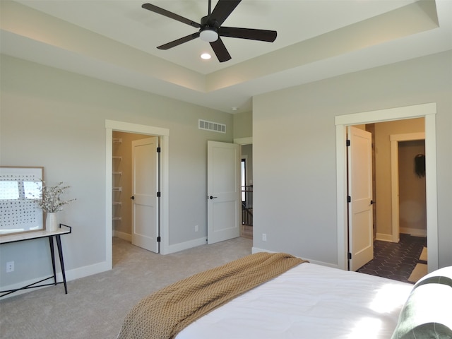 carpeted bedroom with a raised ceiling, ceiling fan, and ensuite bathroom