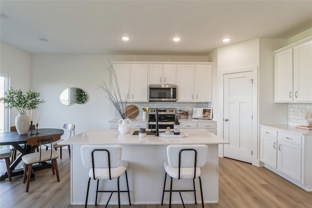 kitchen with appliances with stainless steel finishes, an island with sink, white cabinetry, decorative backsplash, and light hardwood / wood-style flooring